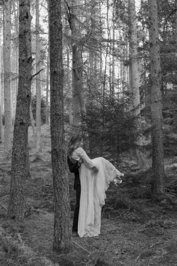 Man carrying his new wife through the forrest in Inverness during their Scotland elopement 