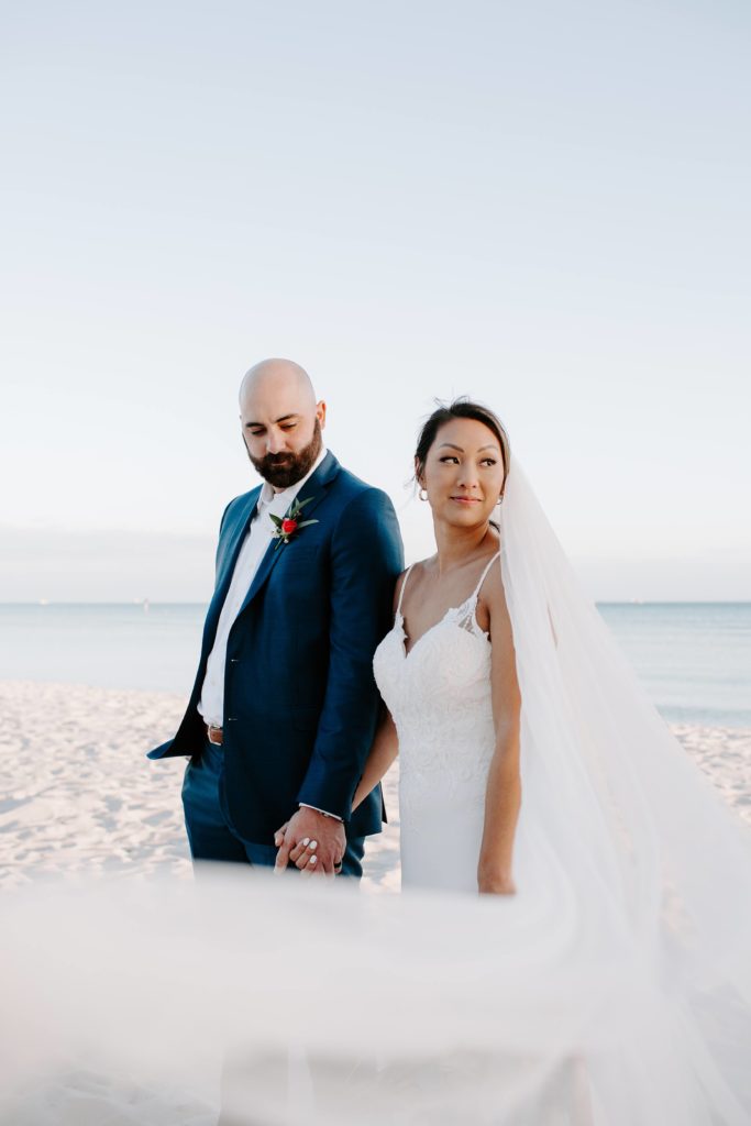 Man holding his new wives hand as she looks off into the distance and her veil blows in the wind during their afternoon intimate key west wedding