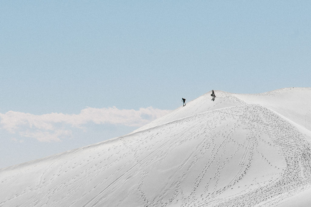 People surfing down sand dunes during their all day adventure elopement at white sand dunes national park in new mexico 