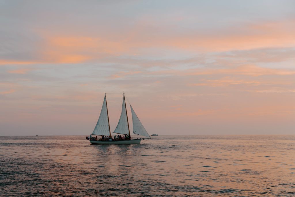 A sail boat sitting out on the ocean as the sunset paints the sky