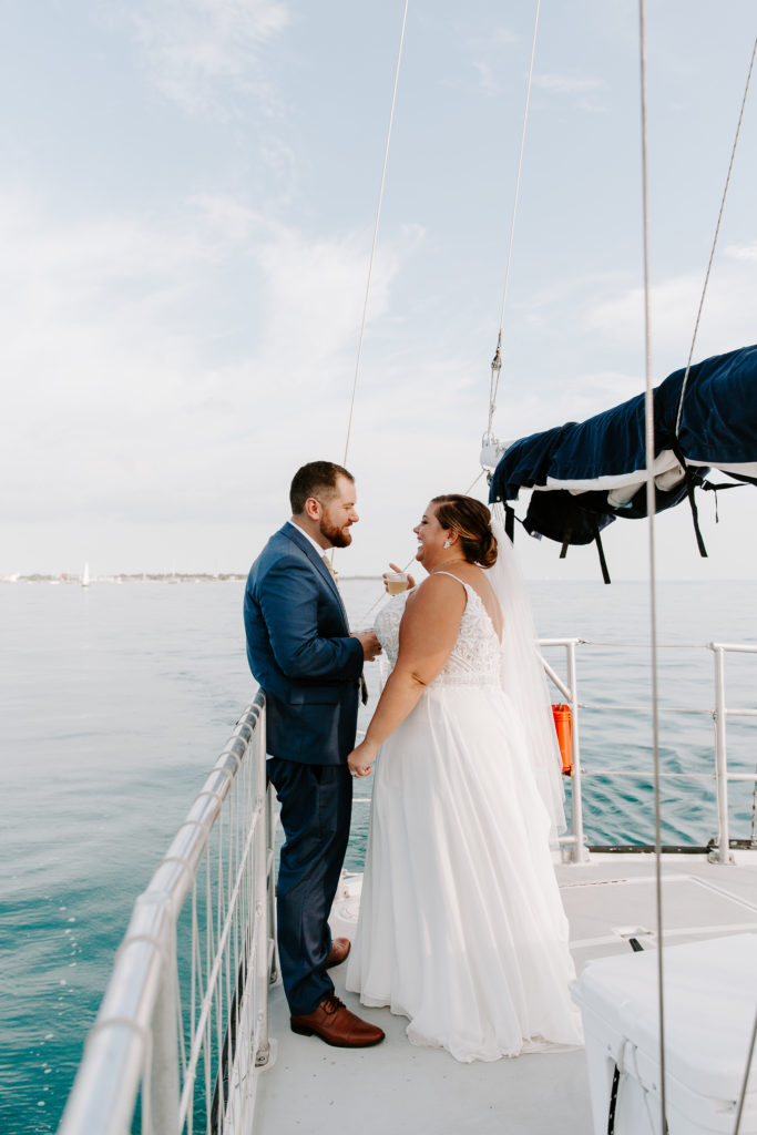 Couple holding champagne looking and laughing at each other on their private sunset cruise during their all day summer key west elopement