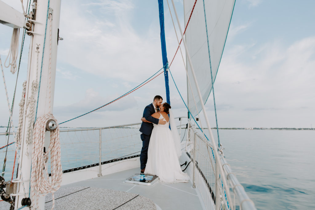 Couple sharing a kiss standing at the front of sail boat during the sunset cruise at the end of their all day elopement in Key West, Florida