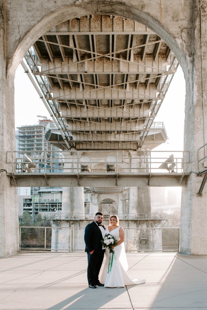 Couple standing next to each other under the pedestrian bridge in Nashville smiling during their Intimate Nashville winter wedding