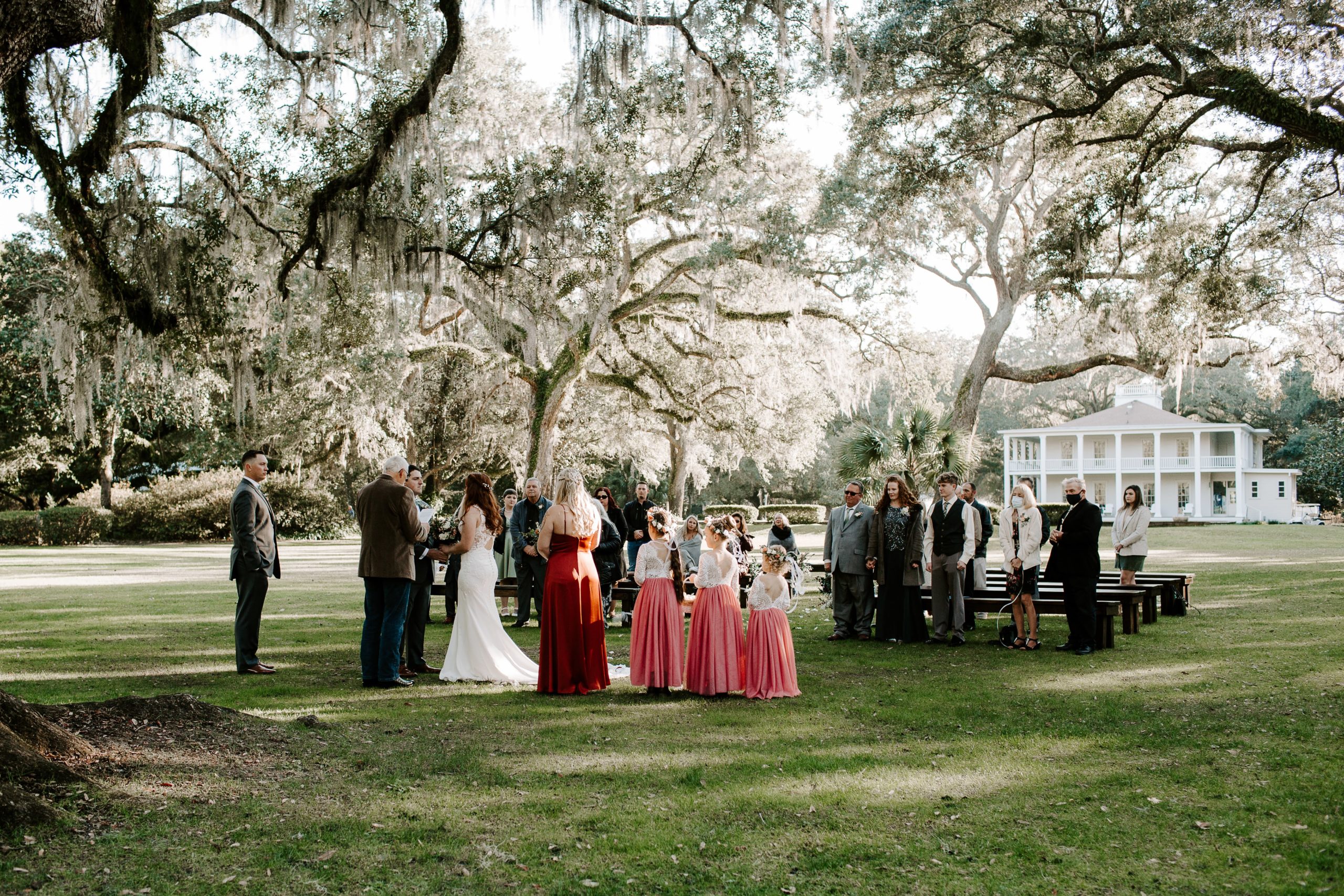 Wedding party and guests standing under a large oak tree as the couple says their vows