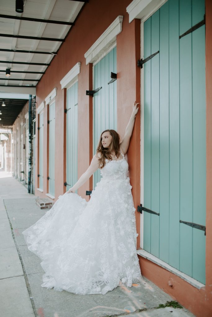 woman throwing her wedding dress as she leans up against a white and blue wall during her all day urban New Orleans elopement