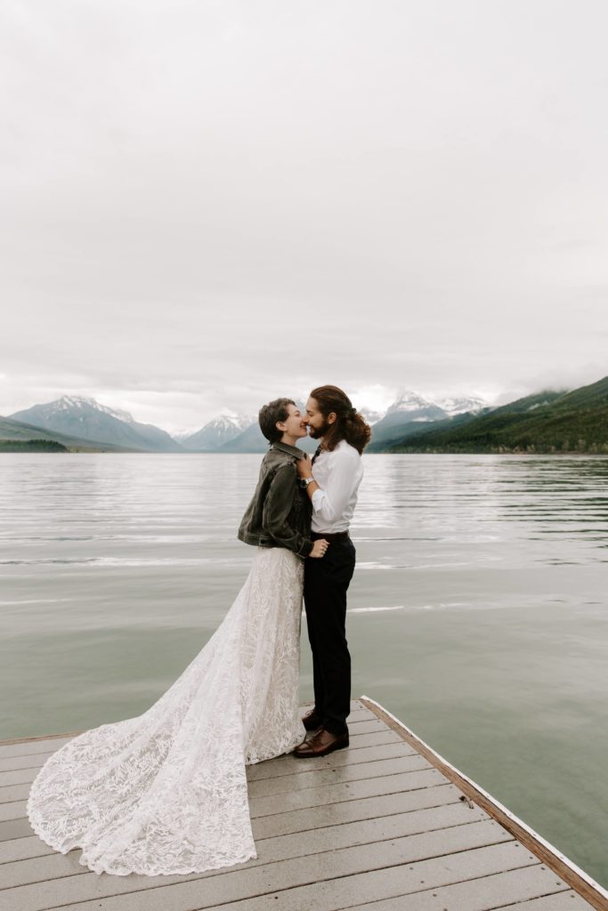 Couple going in for a kiss while standing on a dock on Lake McDonal during their summer Glacier National Park elopement in Montana