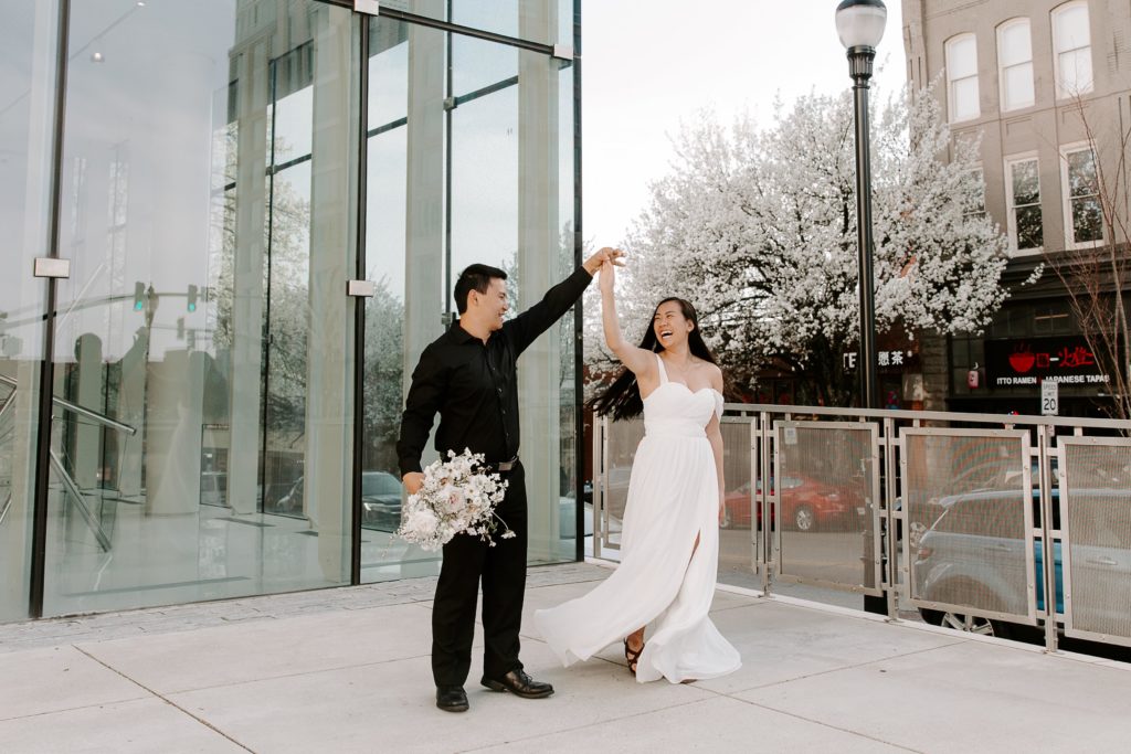 man spinning his partner while he is holding her wedding bouquet and the woman is laughing during their Asheville, North Carolina elopement
