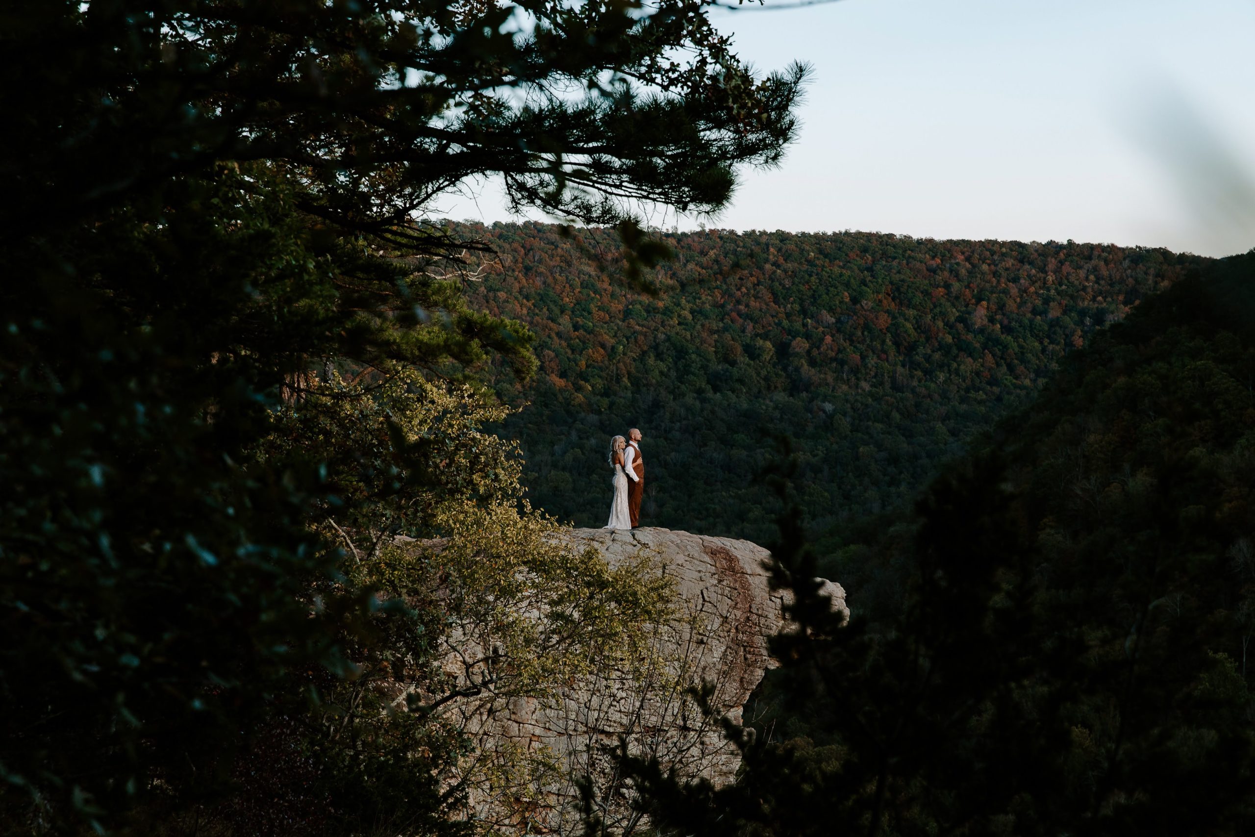 couple standing together on a cliff overlooking trees that are all changing colors during their fall elopement in The Ozarks