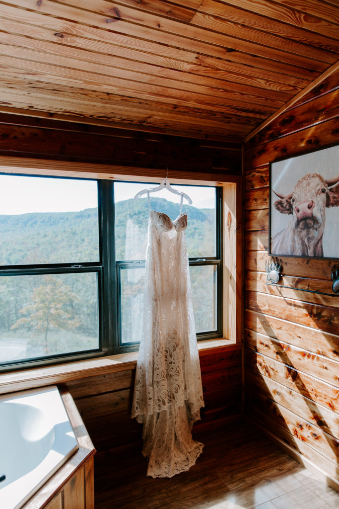 Lace wedding dress hanging in front of a window with the sun beaming in behind it during an Arkansas elopement