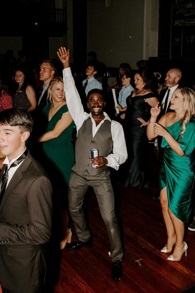Man holding his hand up in the air and smiling as he is dancing at a wedding reception in Mobile, Alabama