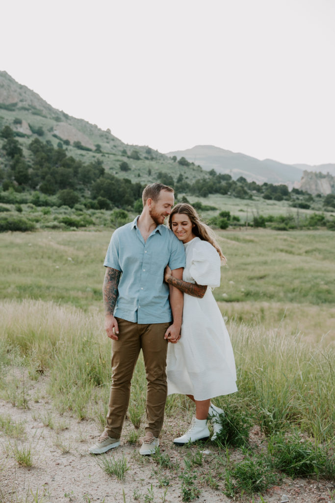 A man and a woman standing in a grass field and the woman is holding onto her partners hand as the man looks down at her during their Colorado Springs couple photos at Garden of the Gods