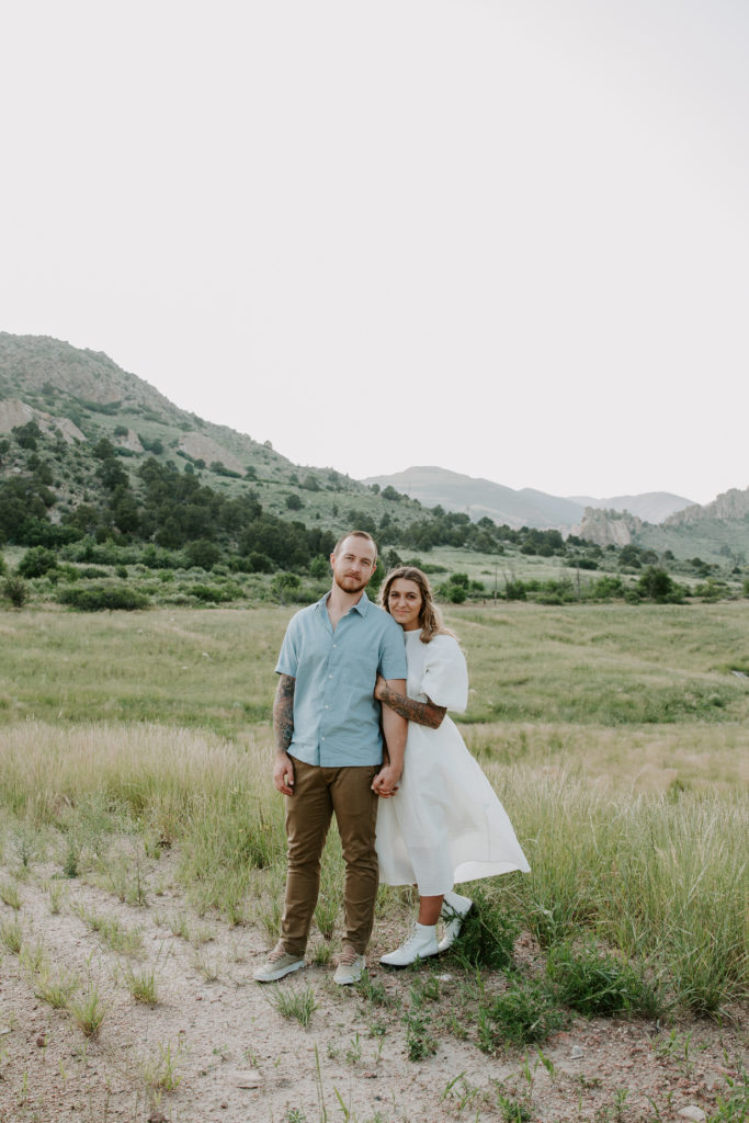 Couple standing in a field with a wide open space behind them and the mountains further back during their Colorado engagement photos