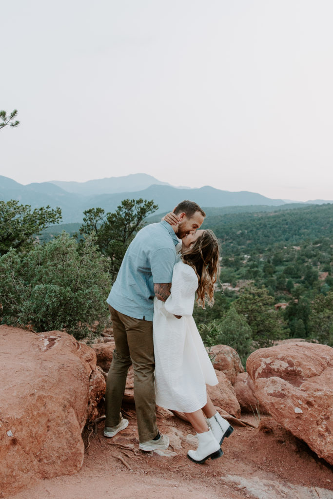 Man dipping his partner and giving her a kiss with the rolling Colorado mountains in the background during their sunset engagement session