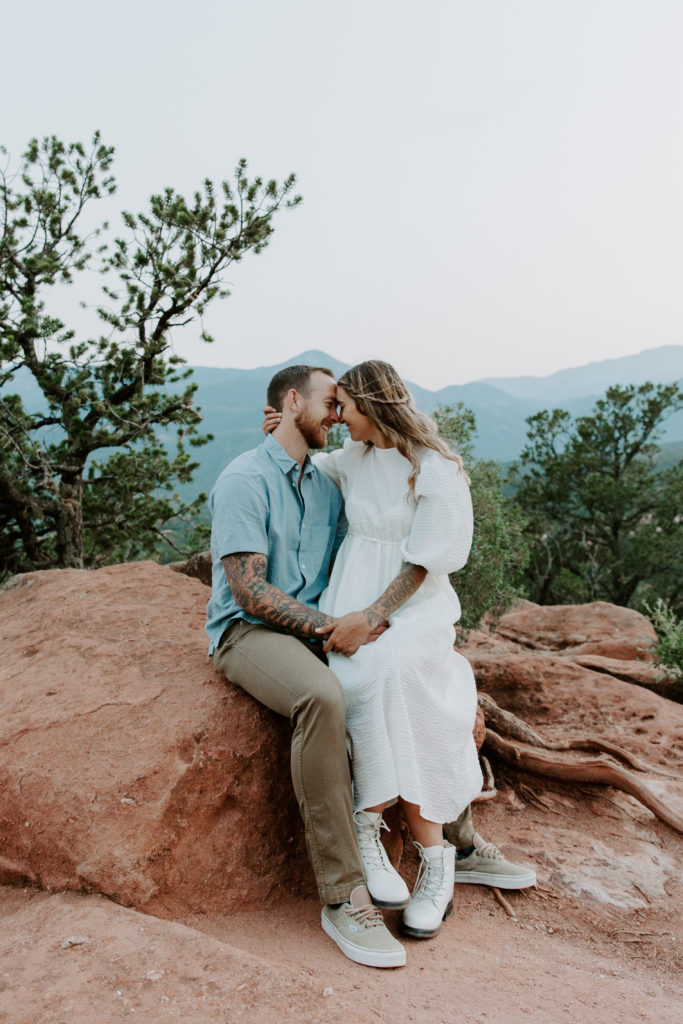Woman sitting on her partners lap as she holds the back of his head and lean their foreheads together during their Colorado Springs engagement session