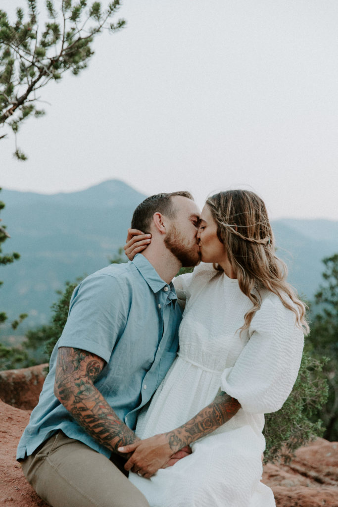 Man and woman sharing a kiss as the woman is sitting on his lap during their Garden of the Gods engagement session
