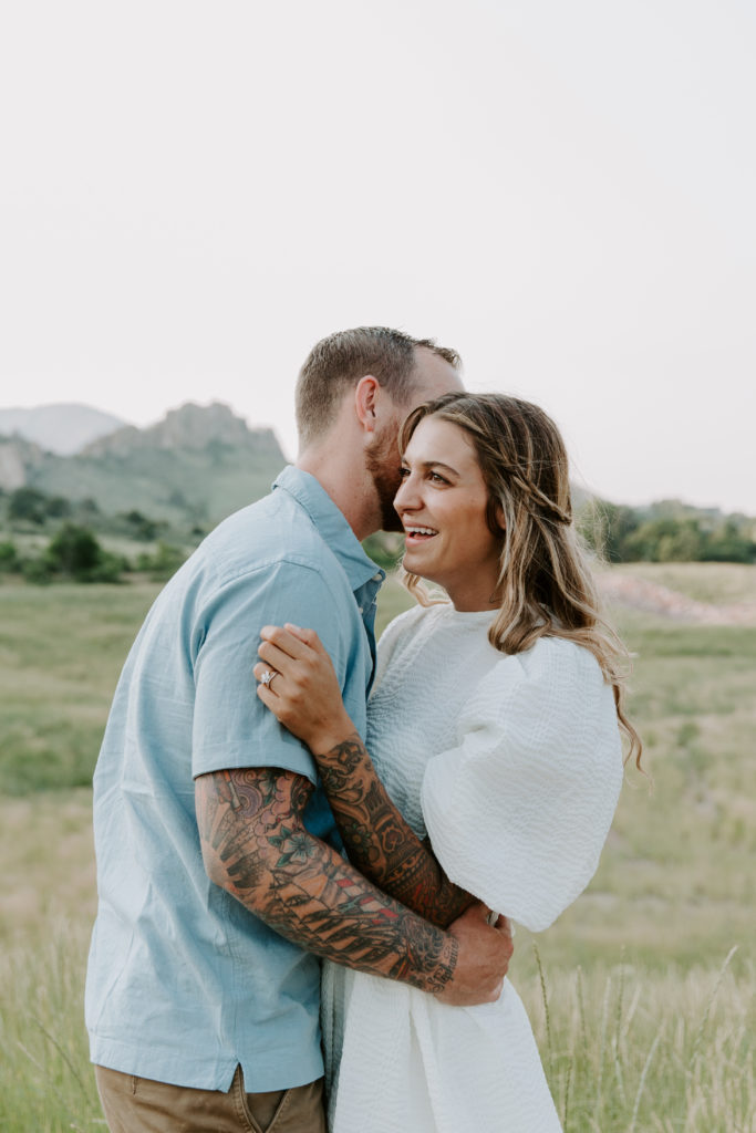 Man whispering into his partners ear as she is laughing during their Colorado engagement photos