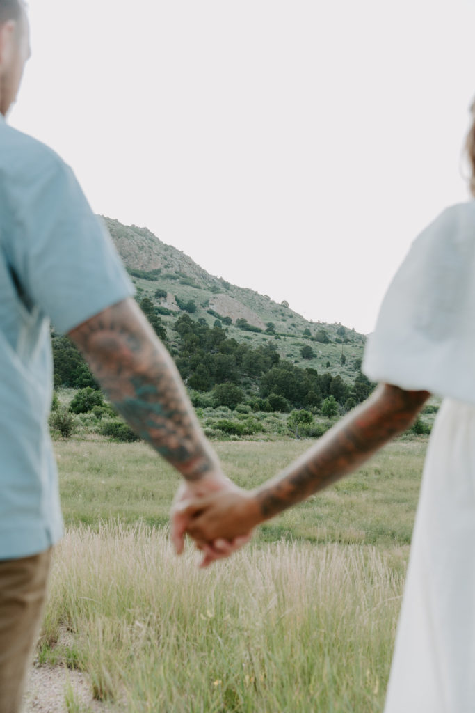 The Colorado mountains are in focus while the couple is holding hands and they are out of focus during their Colorado Springs couple photos