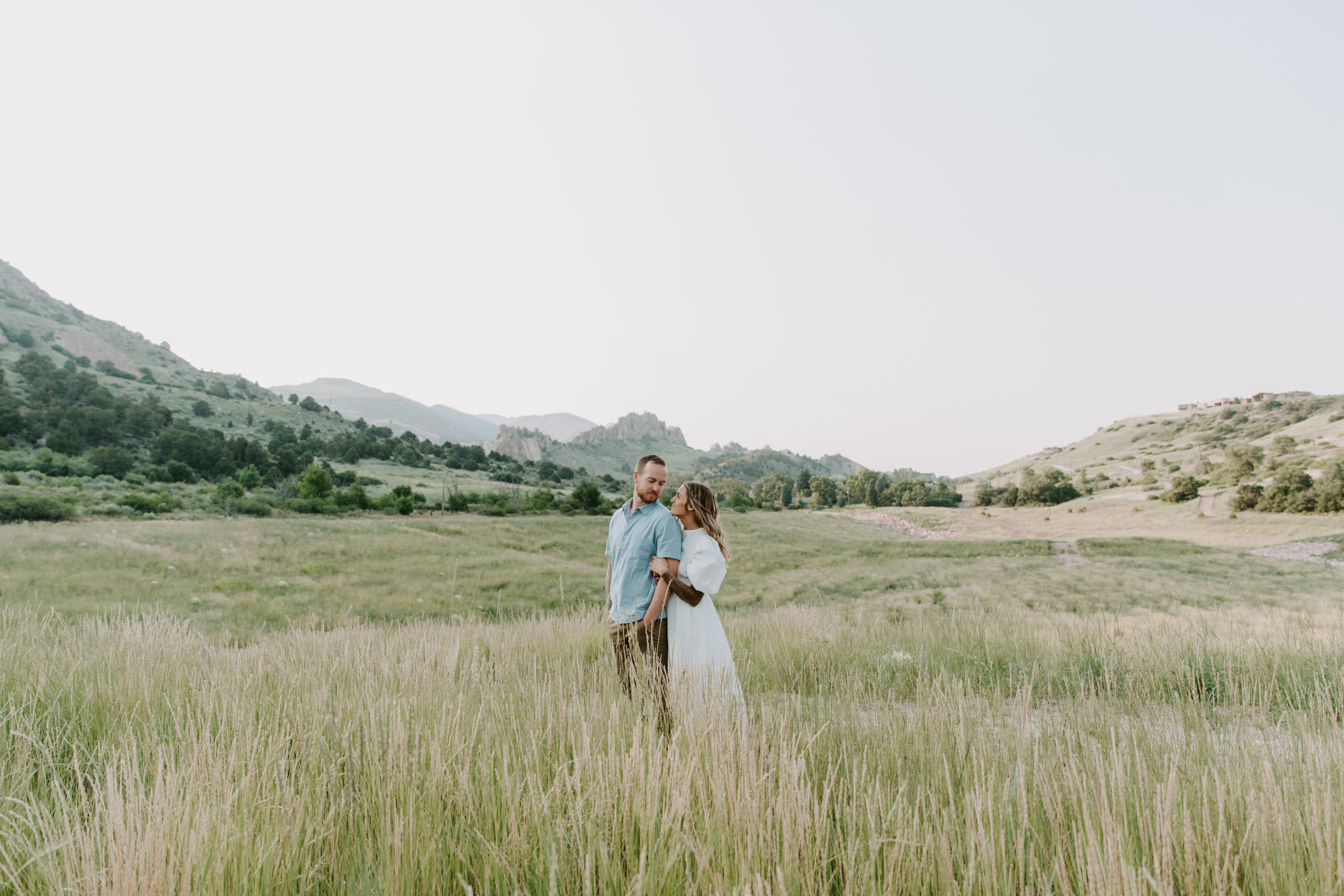 Couple standing in a field as they are looking at each other with the Garden of the Gods in the background during their adventure couple session