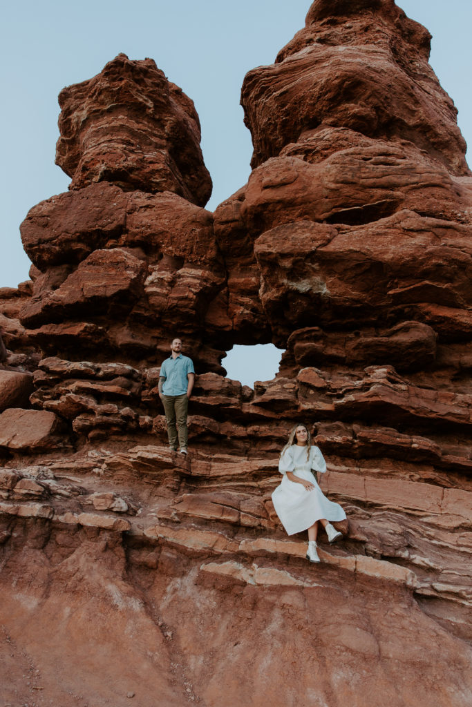A man standing as his partner is sitting on a lower formation in Garden of the Gods during their Colorado Springs engagement photos