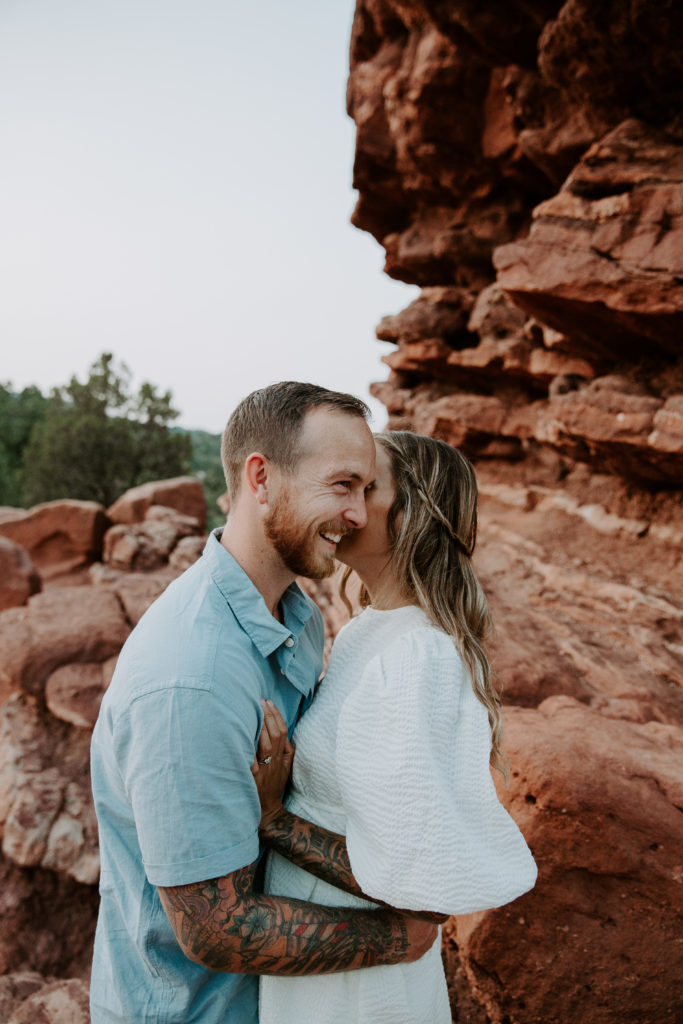 Woman whispering into her husbands ear as he smiles with the red rock formations of Garden of the Gods behind them