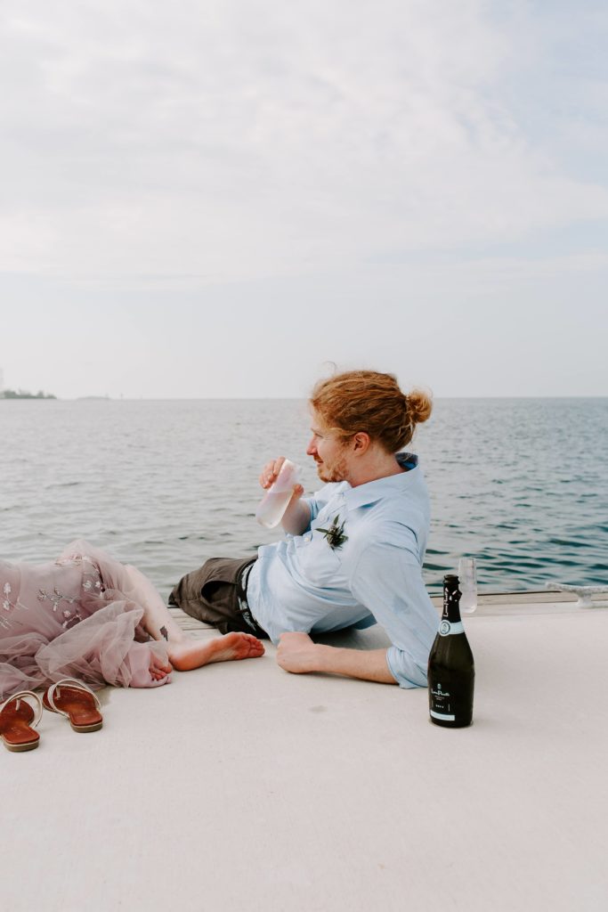 man leaning back on his arms while he is drinking Champagne after their all day florida keys elopement
