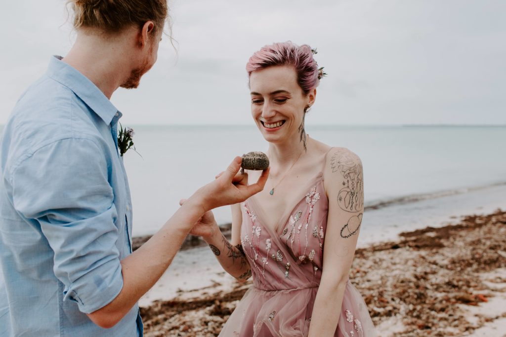 Woman smiling as her partner shows her something he found on the beach during their southern florida elopement