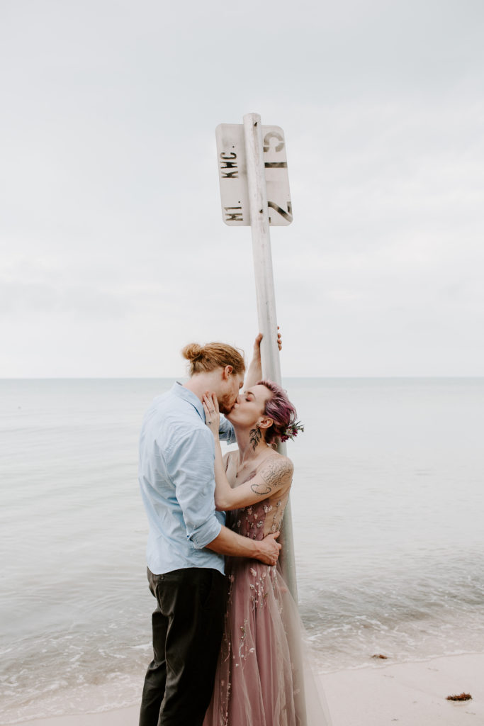 Couple leaning up against a street sign that is on the beach sharing a kiss during their florida keys wedding