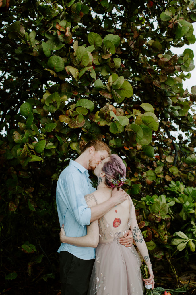 Newly wed couple sharing a kiss with a large tree in front of them during the exploring part of their elopement day