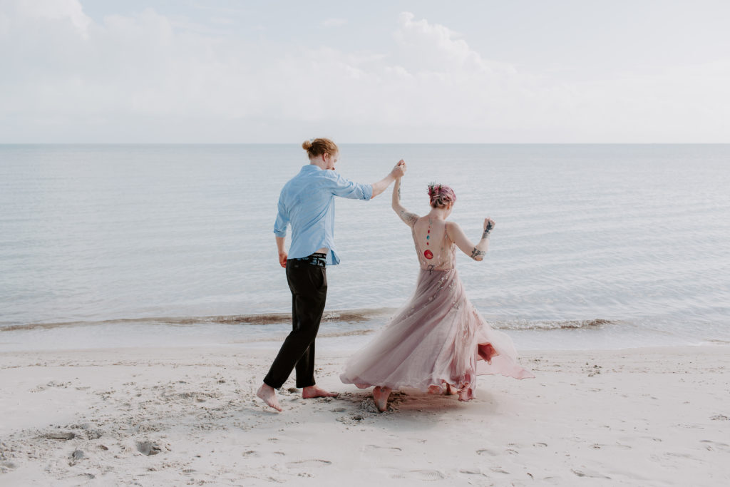 man spinning his parter on the beach as her pink wedding dress spins out during their smathers beach elopement