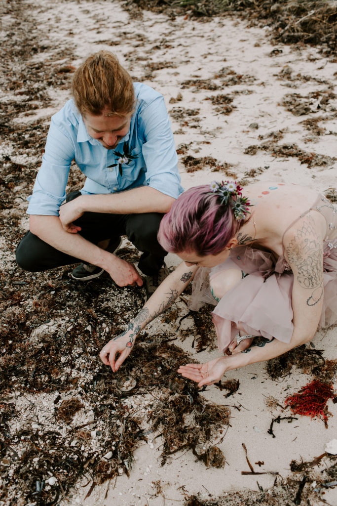Couple bending down examining things that have washed up on the beach during their all day florida elopement