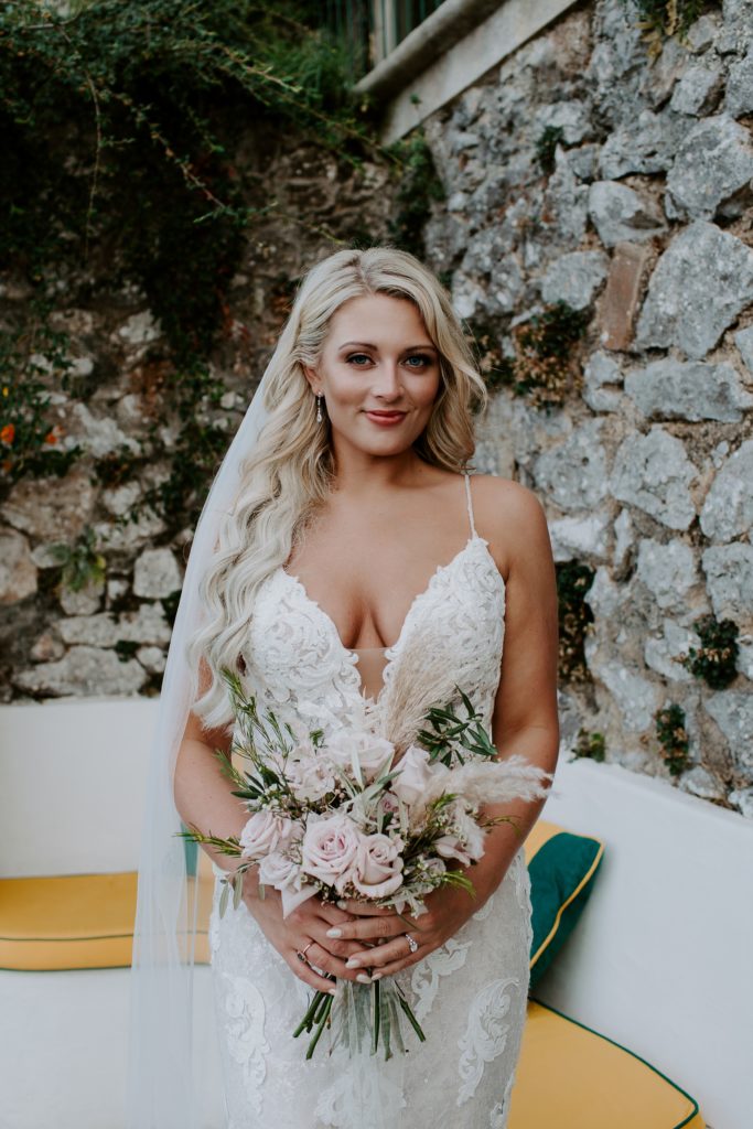 Woman wearing a lace wedding dress and holding her neutral colored bridal bouquet during her Capri, Italy wedding