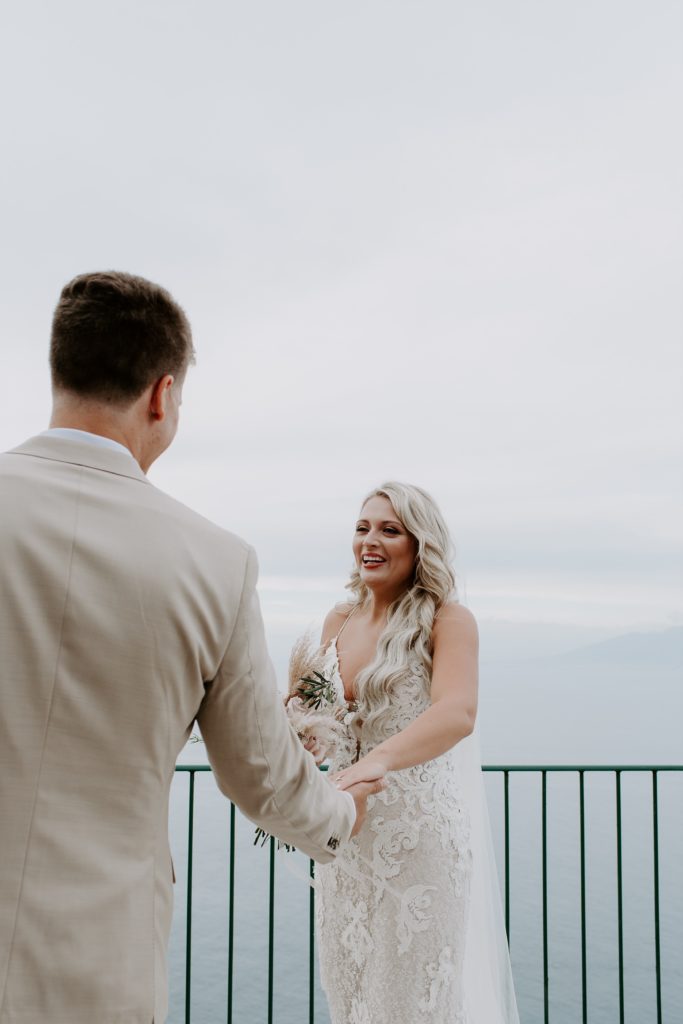 Woman smiling at her partner as he places out his hand for her to grab after their first look on the Amalfi Coast