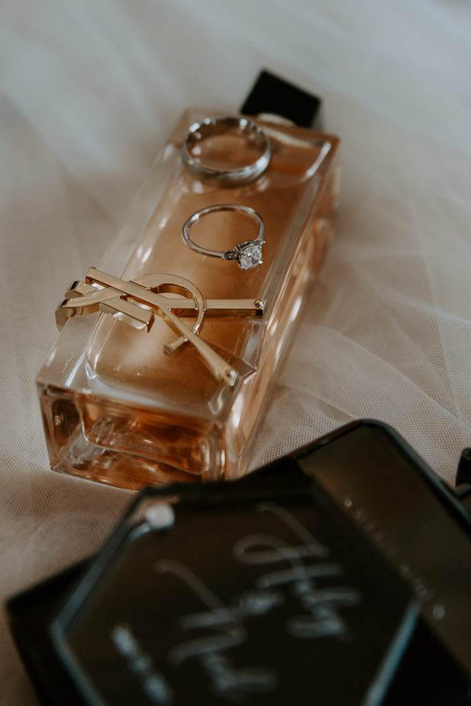 Perfume with wedding bands sitting on top of them with tulle below them all