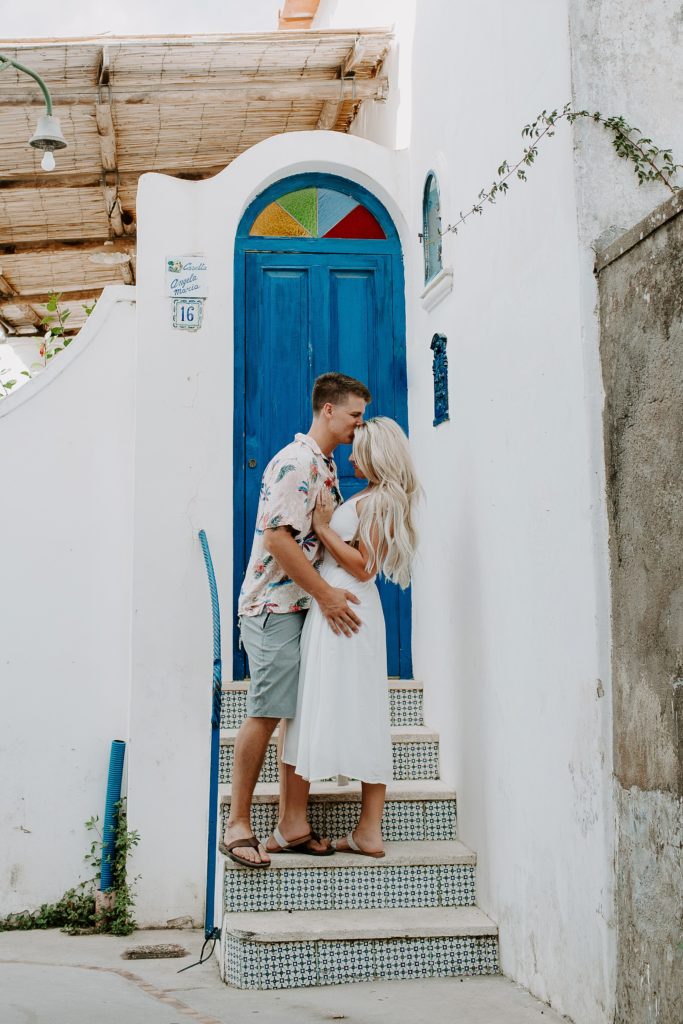 Man kissing his partner on the forehead on stairs in front of a blug door