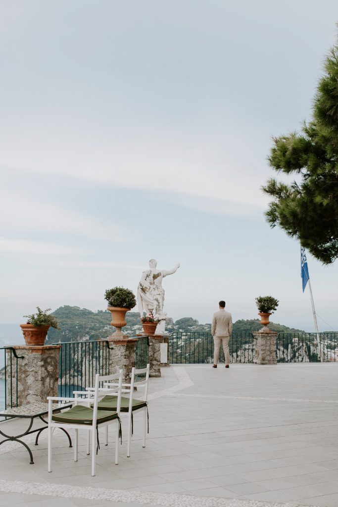 Man standing at the end of the terrace overlook the bay of Naples before his first look with his bride