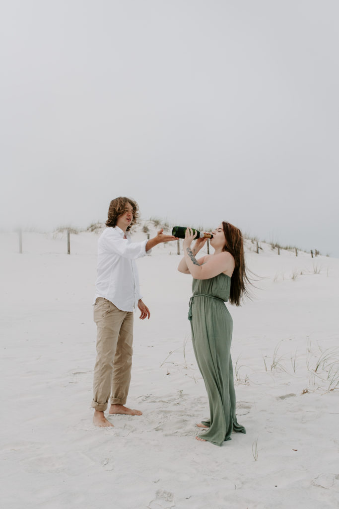 A man tipping the champagne bottle up as his partner is drinking it during their early morning back photos on the emerald coast