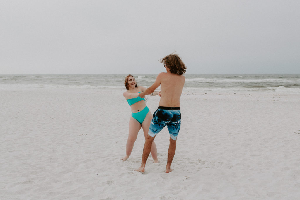 A couple holding hands and spinning in circles laughing during their beach photoshoot