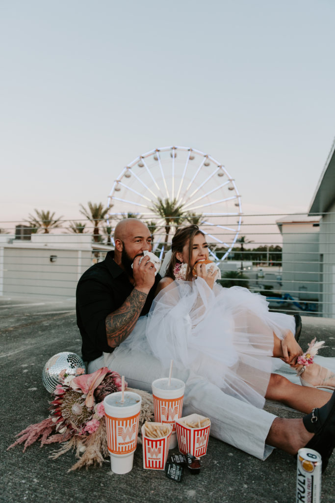 Man and a woman in wedding attire taking big bites of Whataburger as their wedding meal