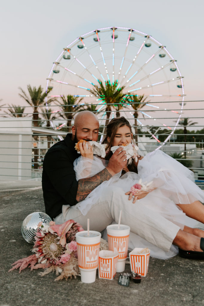 Couple taking big bites of hamburgers and french fries as their wedding day meal 