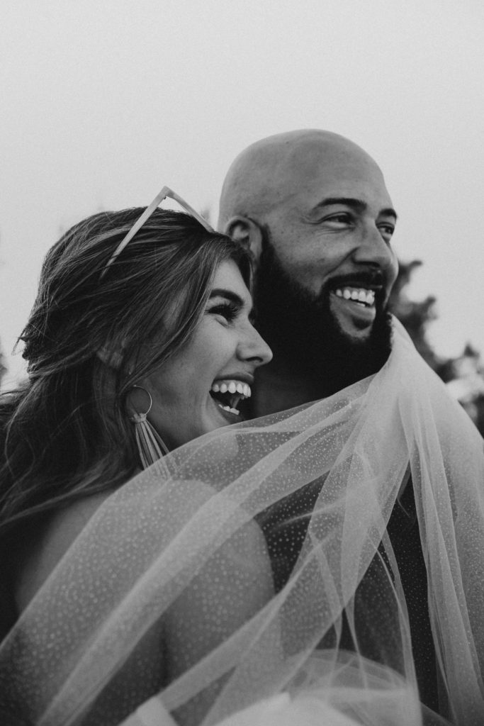 Couple wrapped up in a wedding veil and laughing at something the other said during their Gulf Shores wedding