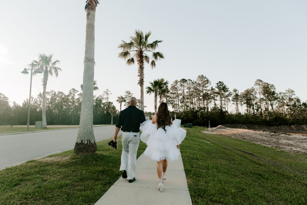 Couple in wedding attire holding hands and walking down a lane of palm trees during their Orange Beach Alabama elopement