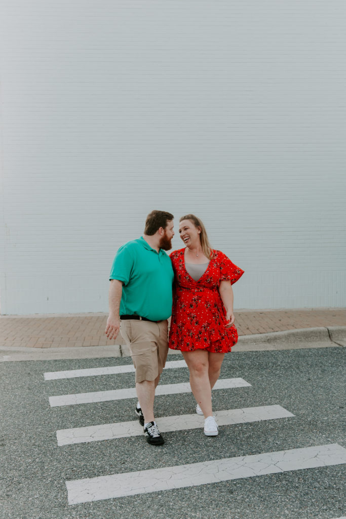 A couple walking across a cross walk looking and laughing at each other during their engagement photos at the Destin Commons
