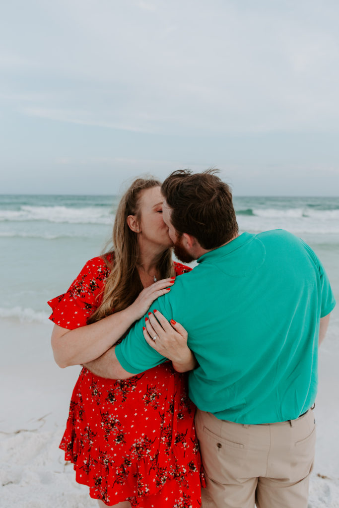 A couple sharing a kiss on the beach as the woman is holding on to her partners arm during their beach engagement photos