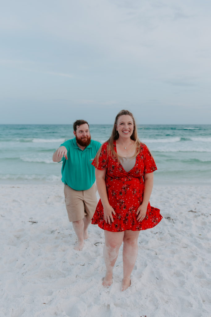 Man sneaking up behind his partner as she is smiling during their beach engagement photos in Destin, Florida