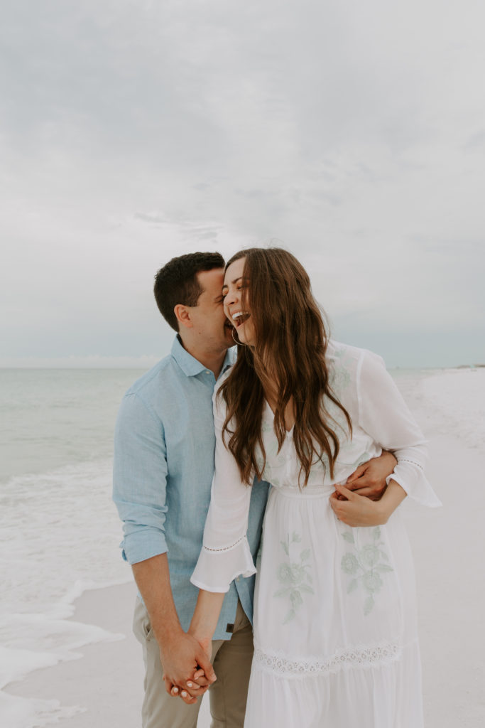 A couple holding hands and the man is whispering into his partners ear making her laugh during their early morning engagement photos