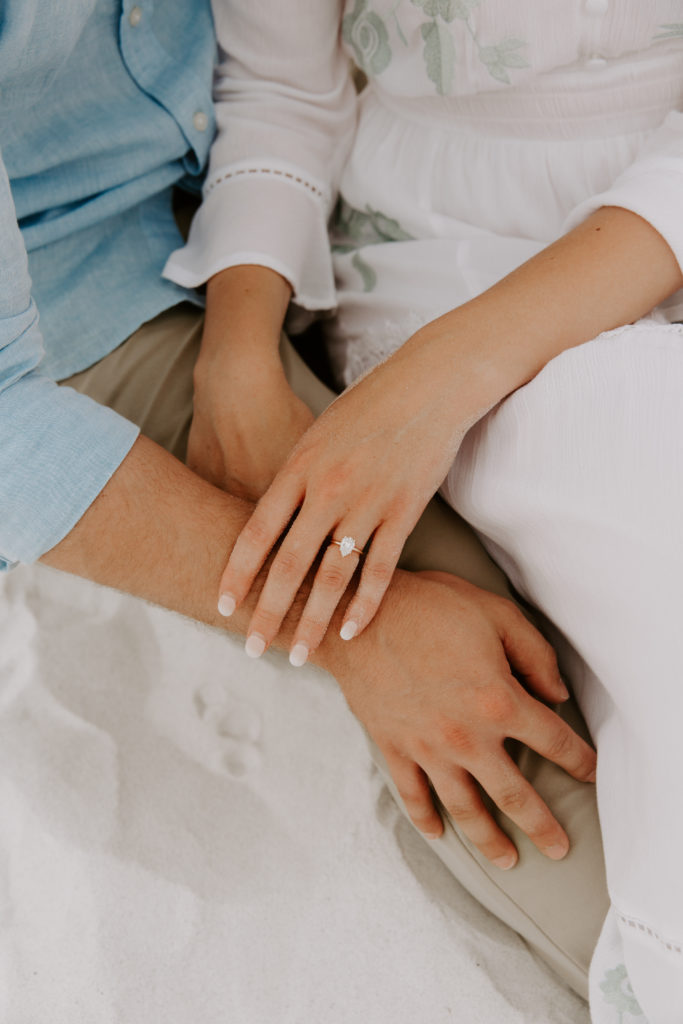 A womans hand holding onto her partners arm showing off her new engagement ring during their early beach couple photos