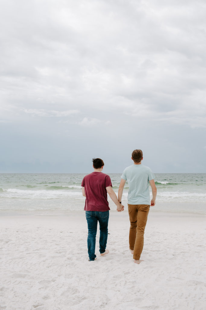 A man and his partner holding hands and walking towards the ocean during their early morning photoshoot