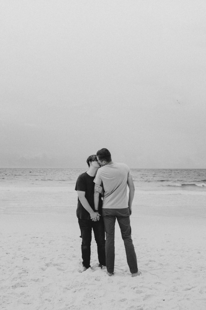 Couple standing on the beach sharing a kiss while holding hands during their Florida panhandle couple photoshoot