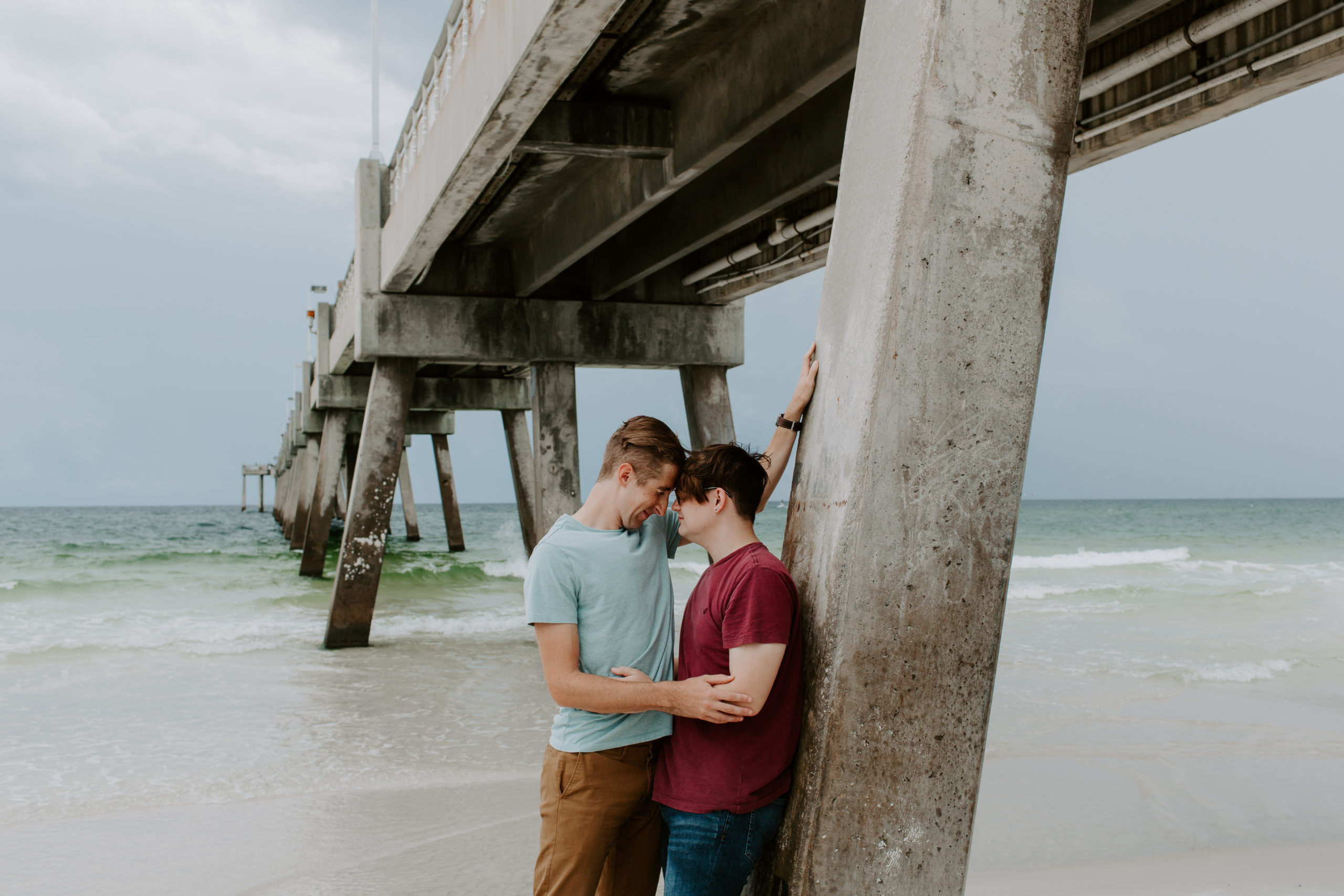 Couple leaning up against the base of the pier with their foreheads resting on the other
