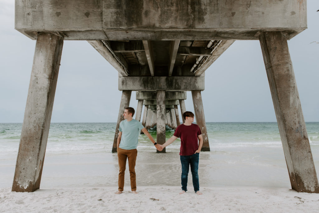 Couple holding hands and standing a few feet apart under the Okaloosa Island Pier during their morning destin photoshoot